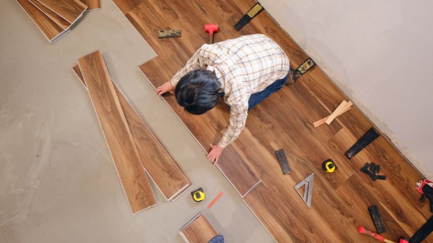 A person working with wooden planks during the installation of solid timber flooring, highlighting craftsmanship and the durability of natural wood.