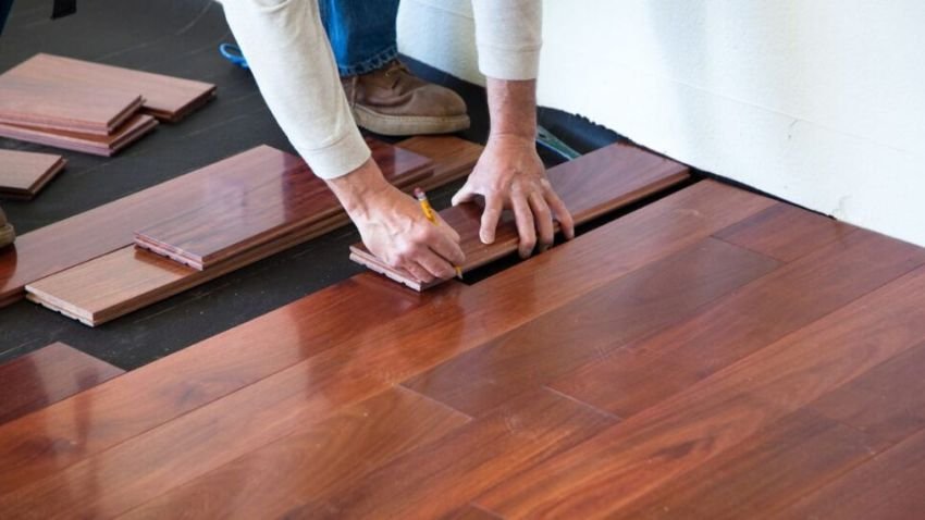 Hands working with wooden planks during the installation of solid timber flooring, highlighting craftsmanship and the durability of natural wood.