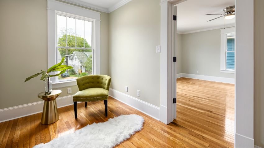 A spacious, sunlit living room with medium-toned laminate floors, large windows, and contemporary furniture. The flooring enhances the room’s warmth and visual harmony.
